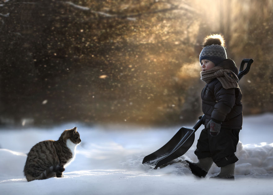 Child with a snow shovel stands near a cat on a snowy farm, capturing a magical scene. Child with a snow shovel stands near a cat on a snowy farm, capturing a magical scene.