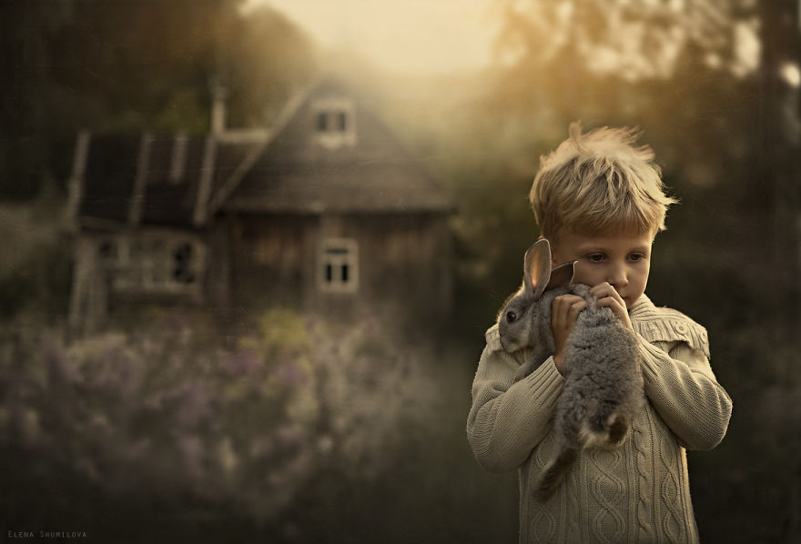 Child holding a rabbit on a Russian farm, with a cozy wooden house in the background. Child holding a rabbit on a Russian farm, with a cozy wooden house in the background.