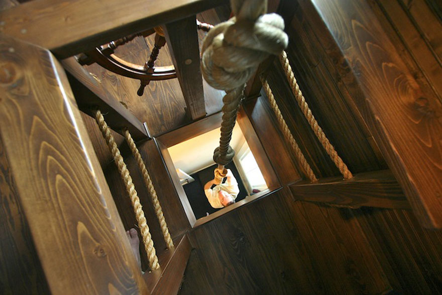 Looking up a wooden ladder with thick ropes in a creative kids room design featuring nautical elements.