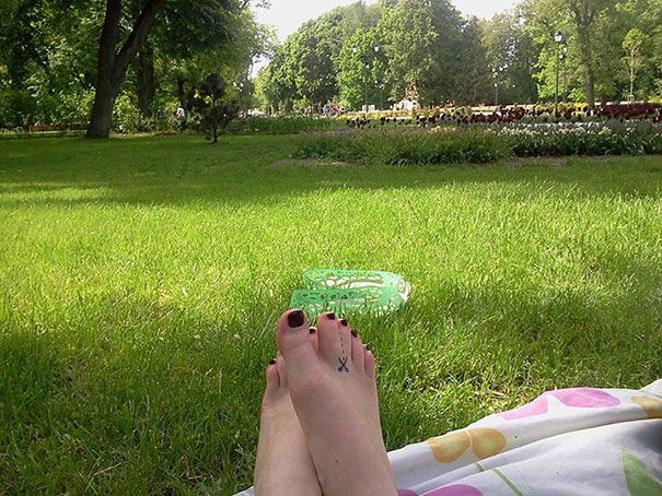 Feet in a park with a creative tattoo on one toe, showcasing clever use of body art.