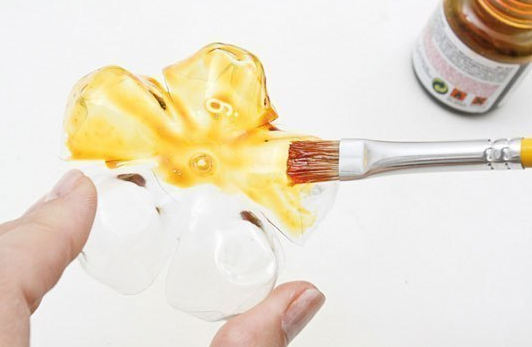 Painting a recycled plastic bottle flower with a brush and yellow paint. Painting a recycled plastic bottle flower with a brush and yellow paint.