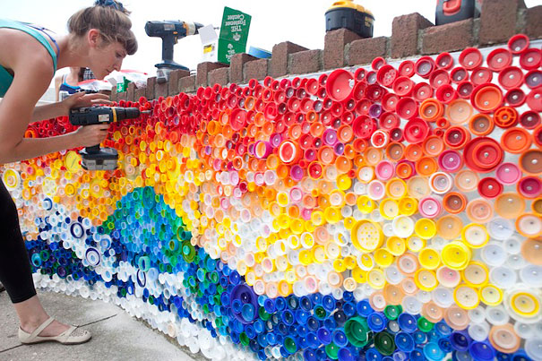 Person creating art with recycled plastic bottles and colorful caps on a wall. Person creating art with recycled plastic bottles and colorful caps on a wall.