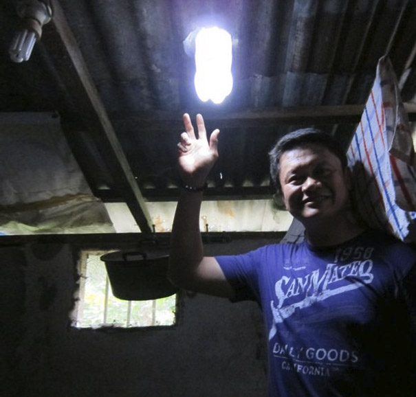 A man smiling under a light made from recycled plastic bottles in a dimly lit room. A man smiling under a light made from recycled plastic bottles in a dimly lit room.