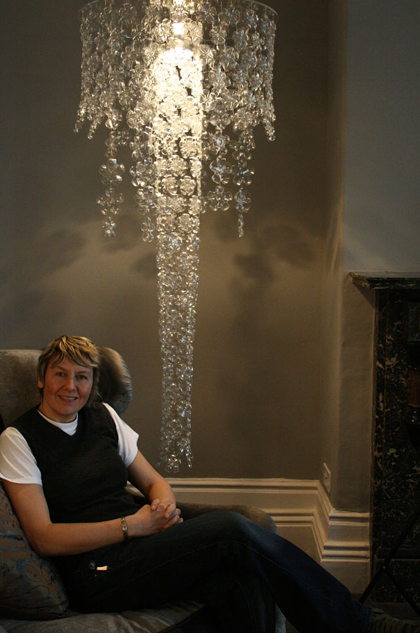 Person sitting under a chandelier made from recycled plastic bottles in a cozy room setting. Person sitting under a chandelier made from recycled plastic bottles in a cozy room setting.