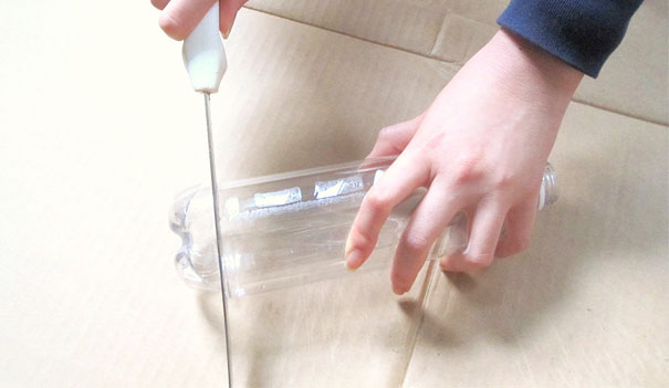 Person cutting a plastic bottle with a knife on cardboard for recycling project. Person cutting a plastic bottle with a knife on cardboard for recycling project.