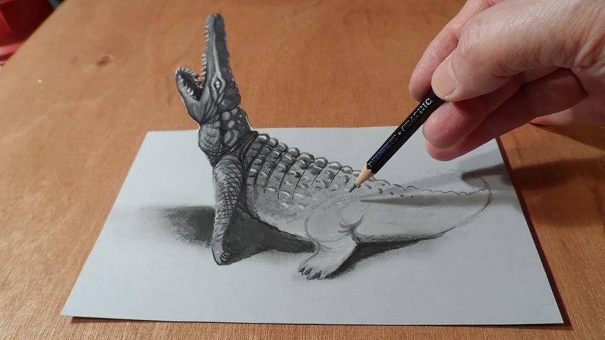 A hand drawing a realistic 3D crocodile on paper, creating an optical illusion. A hand drawing a realistic 3D crocodile on paper, creating an optical illusion.