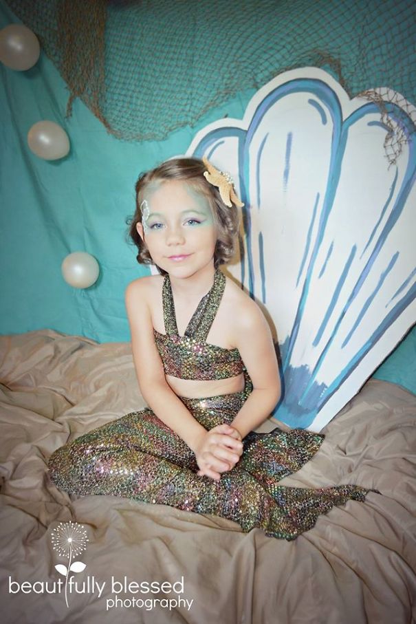 Young girl dressed as a mermaid for children's Halloween costume ideas sitting in front of a shell prop with net decorations.