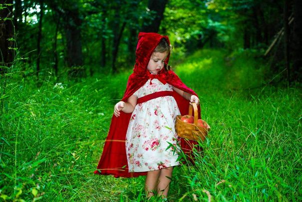 Young child in a red hooded cape and dress holding a basket, showcasing creative children's Halloween costume ideas outdoors.