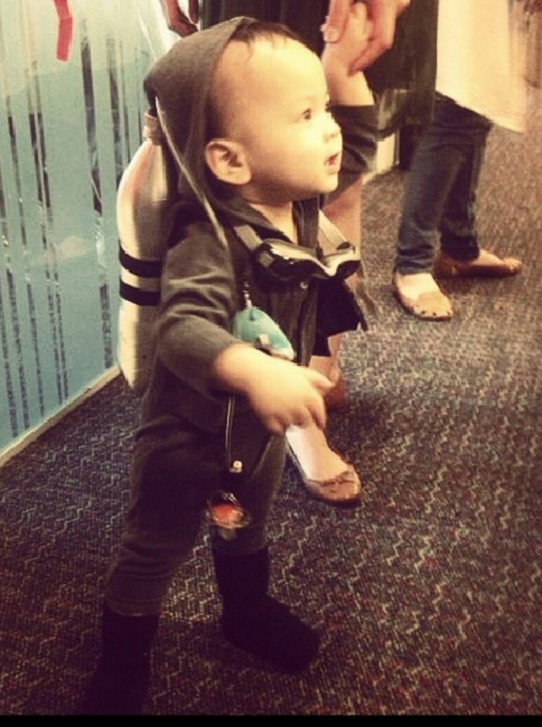 Toddler dressed in a creative Halloween costume with a rocket backpack, holding an adult's hand indoors.