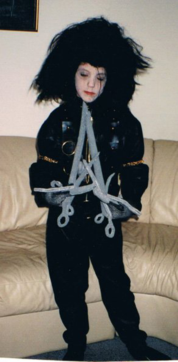 Child in an elaborate Halloween costume with black outfit, large wild wig, and gray scissor prop for children's Halloween costume ideas.