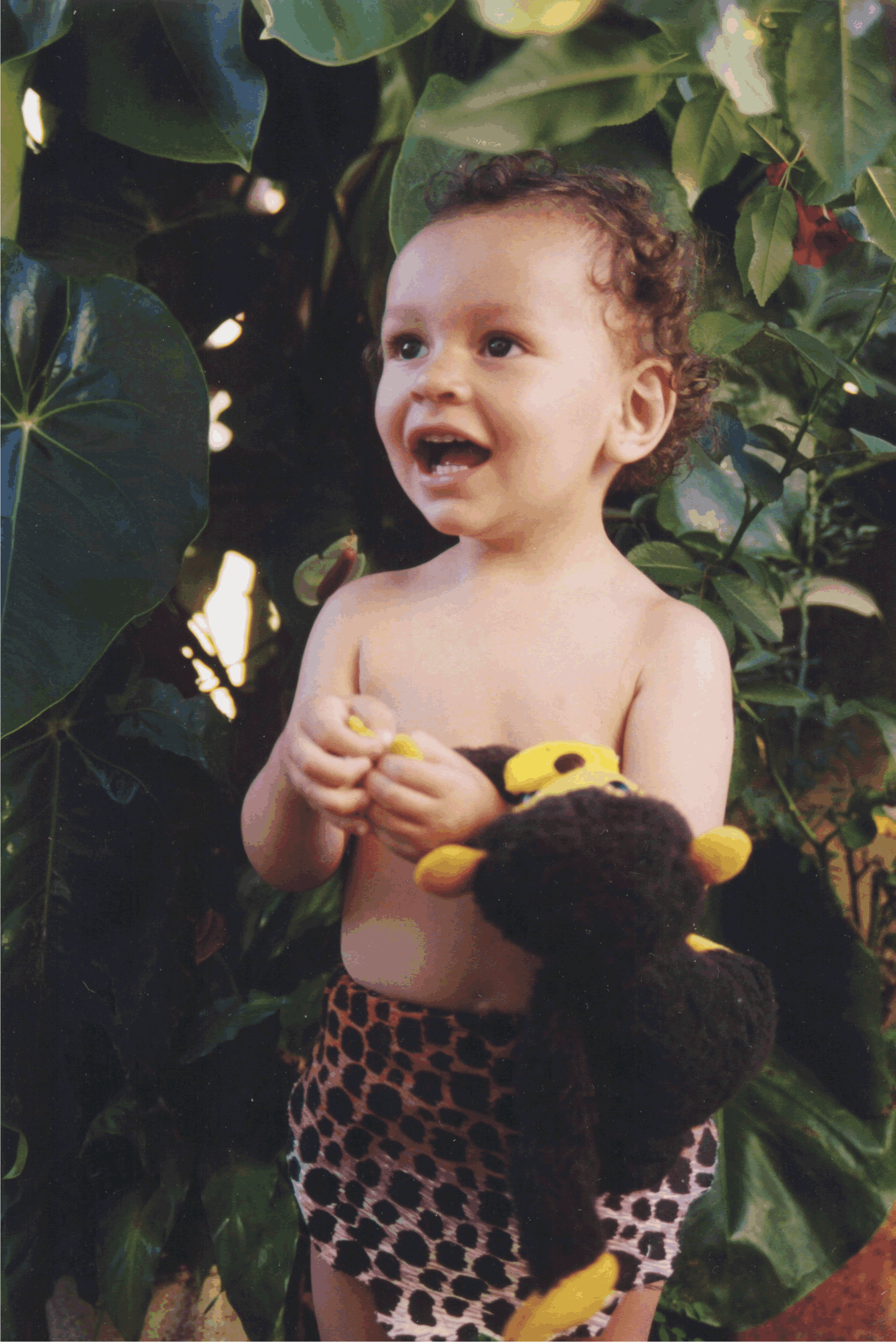 Young child in a Halloween costume holding a stuffed animal, surrounded by green foliage for children Halloween costume ideas.