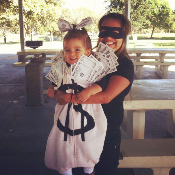 Two children dressed in creative Halloween costume ideas, one as a money bag with fake bills and the other wearing a black mask.