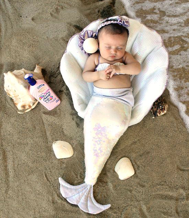 Baby dressed as a mermaid in a shell on the sand, an adorable children's Halloween costume idea for toddlers.