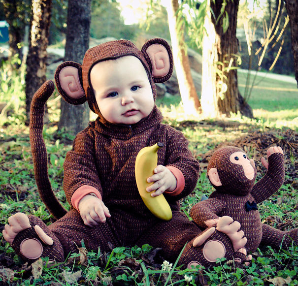 Baby dressed in a monkey costume holding a banana, sitting outdoors as part of children's Halloween costume ideas.