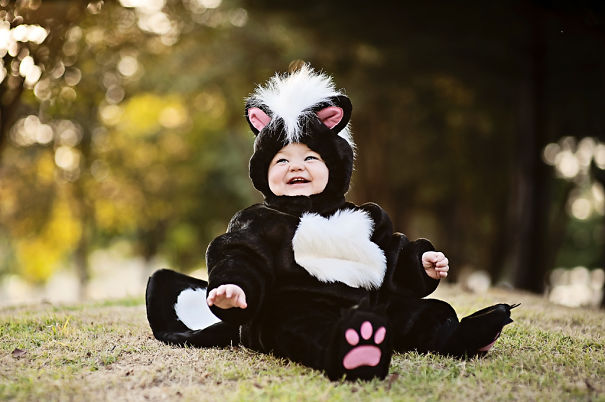 Baby dressed in a cute skunk costume sitting outdoors, perfect for children’s Halloween costume ideas celebration.