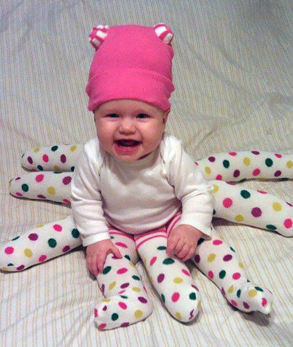 Smiling baby dressed in a creative children's Halloween costume with colorful polka-dot spider legs and a pink hat.