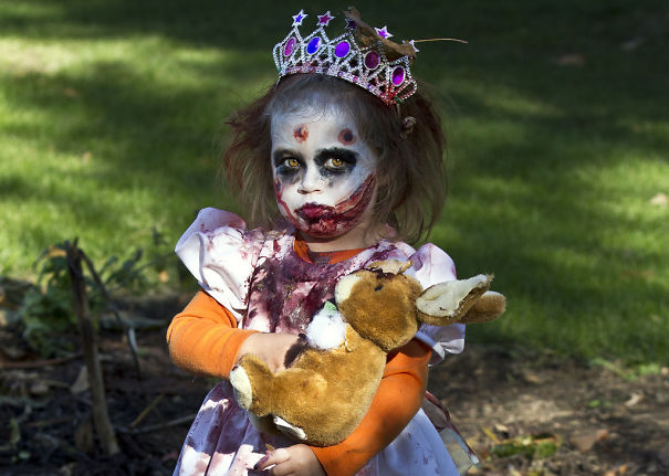 Child in creepy princess costume with detailed Halloween makeup holding a stuffed rabbit outdoors Halloween costume ideas.