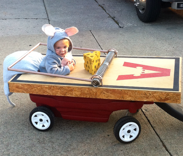 Child in a mouse Halloween costume sitting inside a wagon designed as a giant mousetrap, creative children's Halloween costume idea.