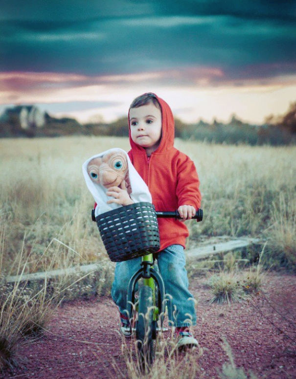 Child wearing a red hoodie riding a bike with an E.T. doll in the basket, a creative children's Halloween costume idea.