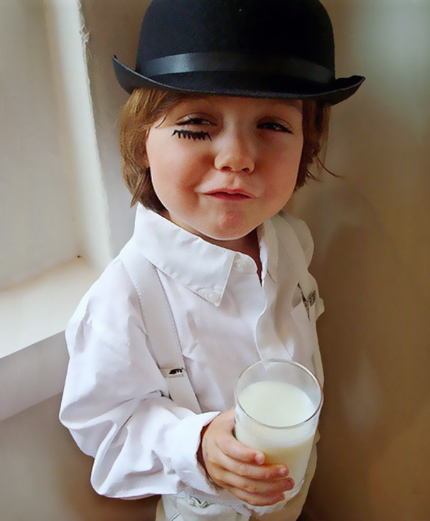 Child dressed in a Halloween costume wearing a black bowler hat and white outfit holding a glass of milk for children's Halloween costume ideas.