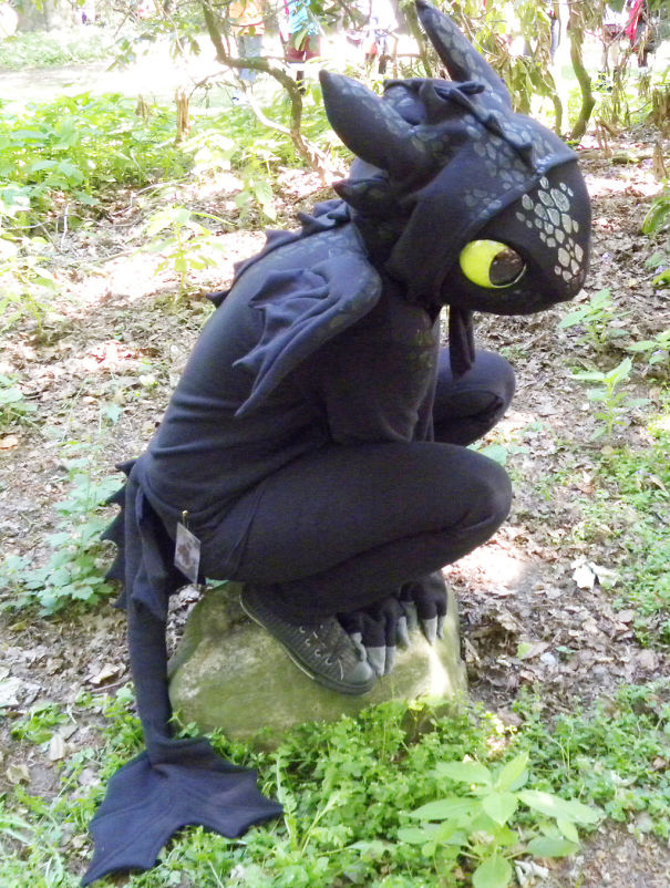 Child wearing a detailed dragon costume crouching on a rock in a forest, a unique children's Halloween costume idea.