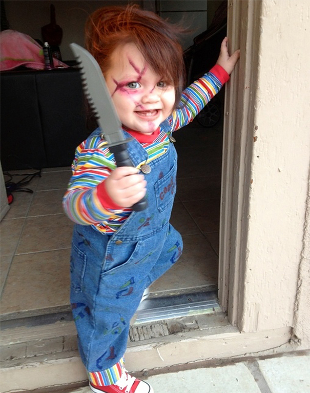 Toddler wearing a scary children’s Halloween costume with face paint and holding a toy knife at a doorway.