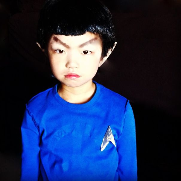 Child in children's Halloween costume ideas wearing blue shirt with pointed ears and dark hair against black background.