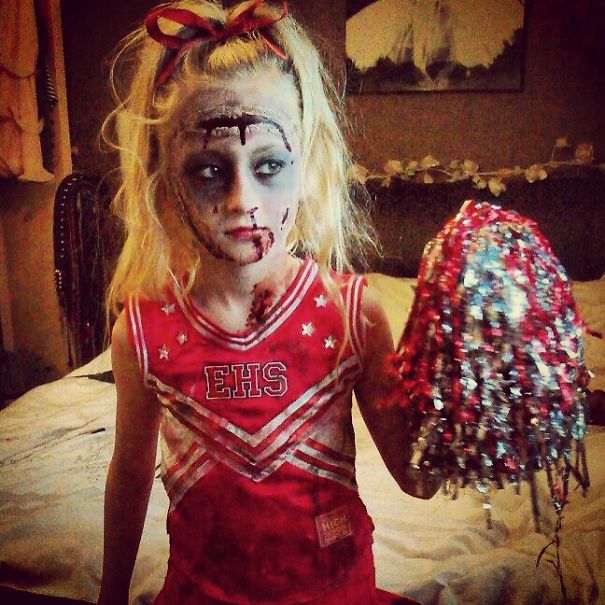 Child dressed in a zombie cheerleader costume holding pom-poms, showcasing children's Halloween costume ideas.