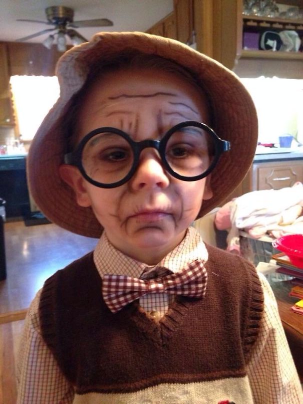 Child in Halloween costume wearing round glasses, hat, bow tie, and face paint showing wrinkles for a costume idea.