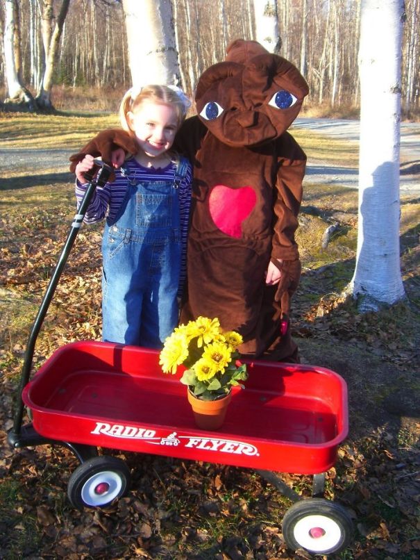 Two children outdoors with one wearing a Halloween costume standing next to a red wagon and flowers children's Halloween costume ideas.