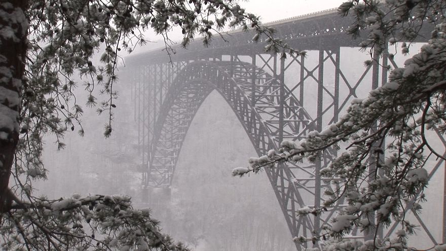 Mystical bridge with arch design covered in snow, surrounded by frosted trees creating an otherworldly winter scene.