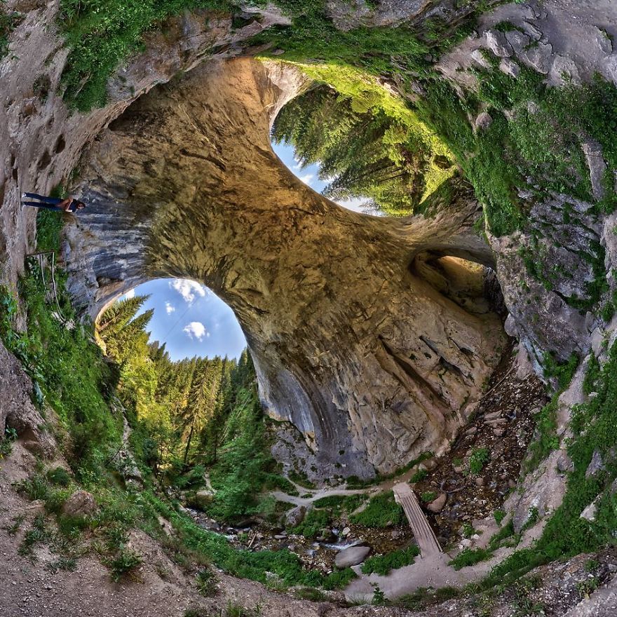 Mystical natural stone bridge with lush greenery and a small stream beneath, creating an otherworldly landscape scene.