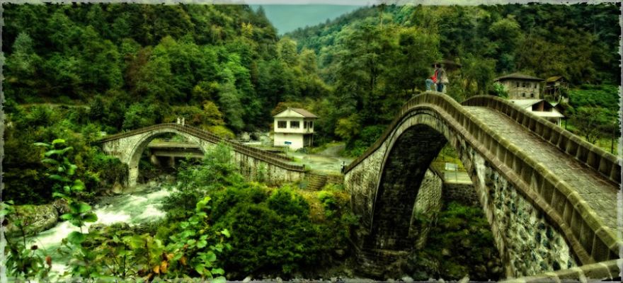 Mystical stone bridges arching over a river surrounded by lush green forest and mountainous landscape.