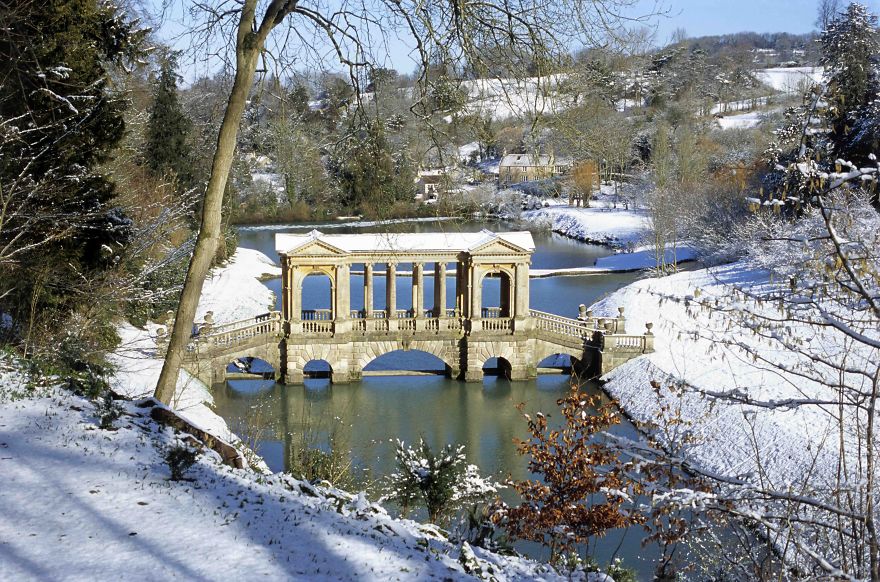 Stone bridge with classical columns over a river in a snowy landscape, showcasing mystical bridges in winter.