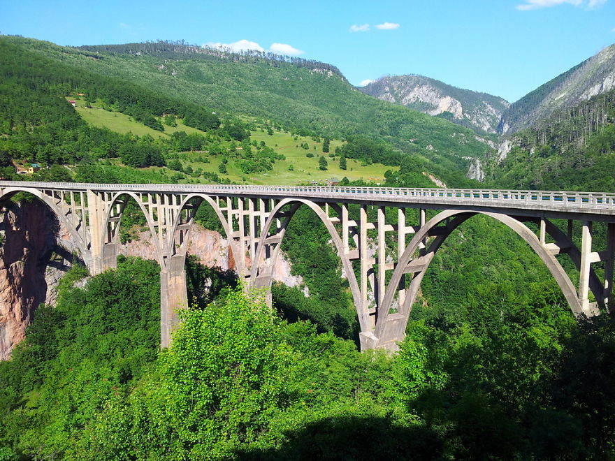 Arch bridge surrounded by lush greenery and mountains, showcasing mystical bridges connecting natural landscapes.