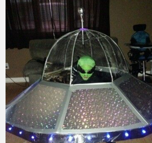 Child wearing a creative children's Halloween costume idea as an alien inside a DIY UFO spaceship indoors.