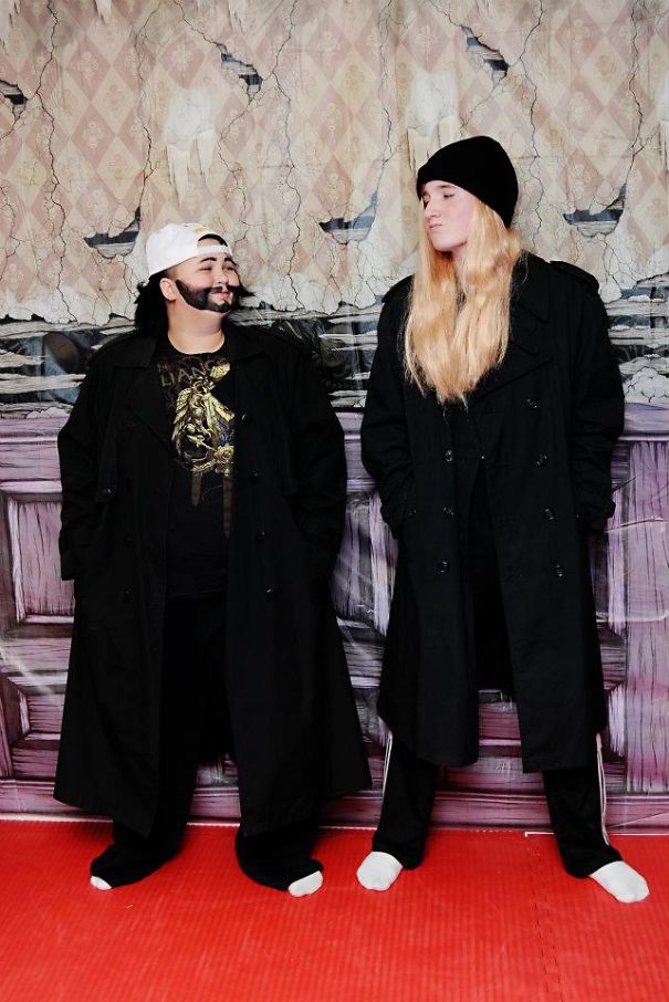 Two kids wearing Halloween costume ideas in black coats and hats against a spooky worn wall background.