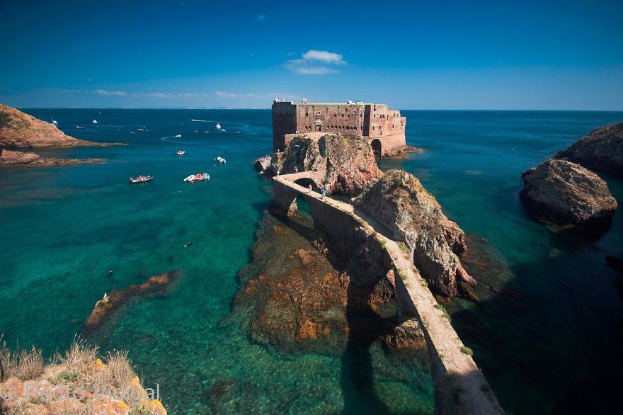 Mystical bridge connecting rocky islands over clear blue water under a bright sky, evoking a magical otherworldly journey.