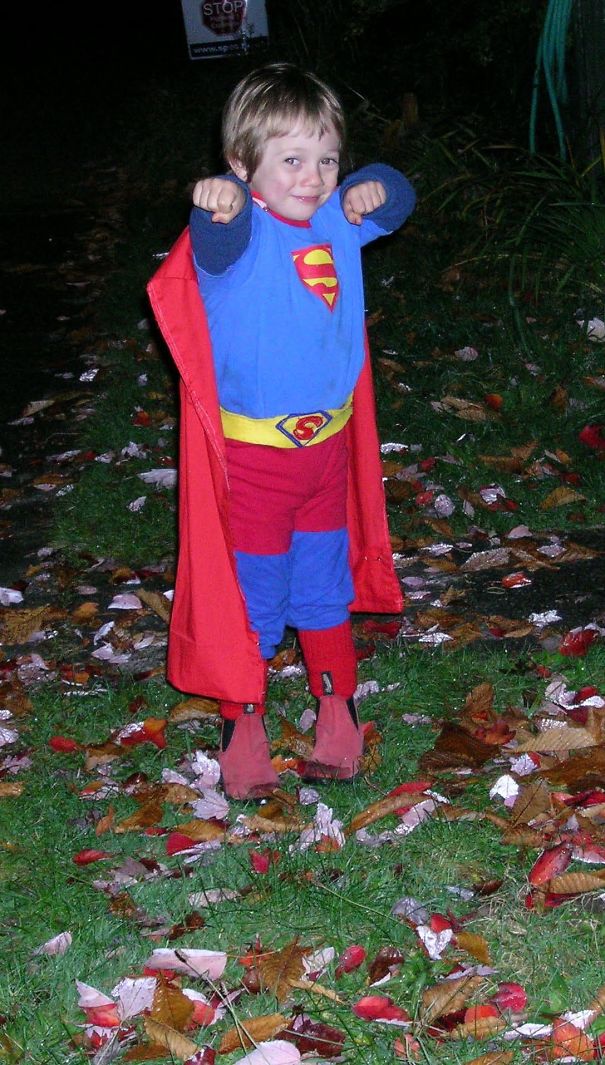Child dressed in a homemade superhero costume posing outdoors on a leaf-covered ground for Halloween costume ideas.