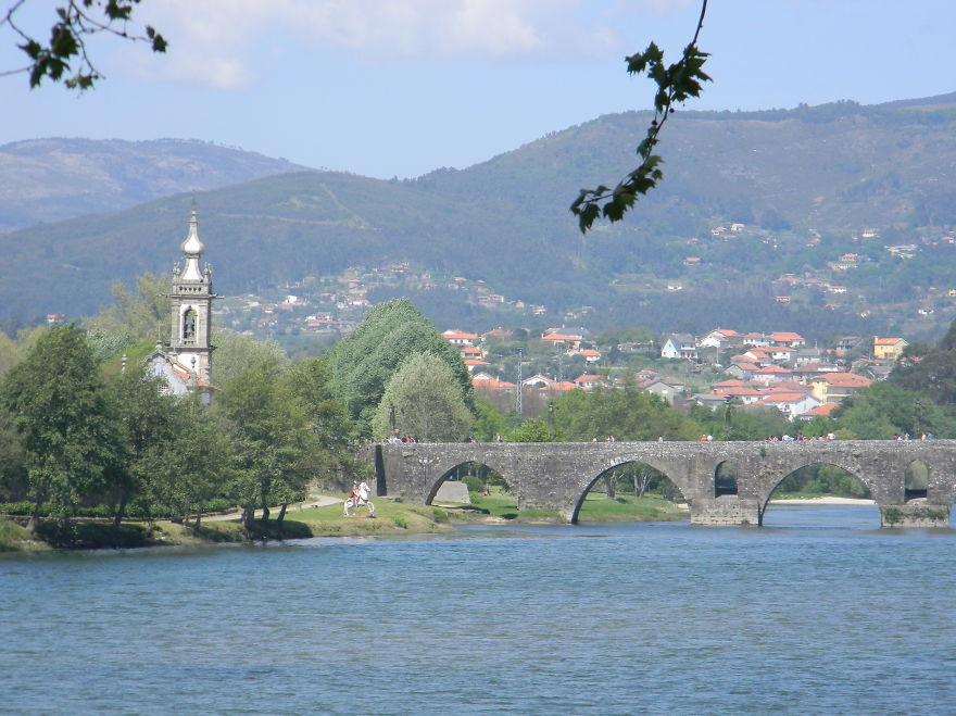 Stone mystical bridge over river with village and mountains in the background on a clear sunny day