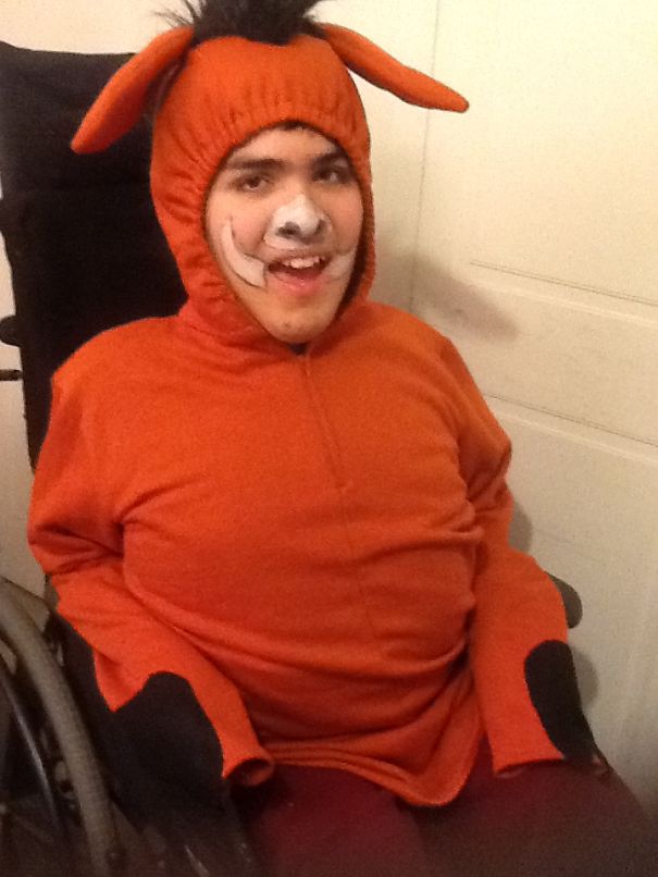 Child in an orange Halloween costume with face paint and bunny ears, smiling while seated in a wheelchair for costume ideas.
