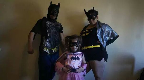 Family dressed in children's Halloween costume ideas as superheroes posing against a plain background.