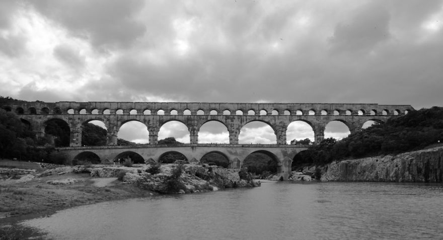 Ancient mystical stone bridge spanning a river under a dramatic cloudy sky in a natural landscape setting.