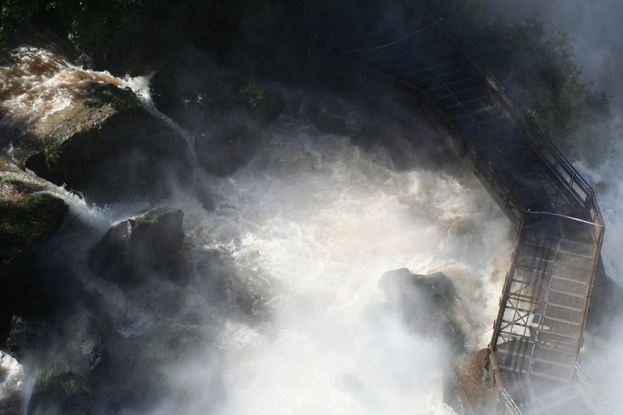 Wooden mystical bridge shrouded in mist over rushing river waters and dark rocks in a foggy natural landscape.