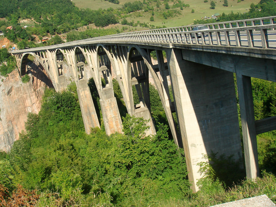 Concrete mystical bridge with arches spanning a lush green valley, surrounded by dense trees in a scenic natural setting.