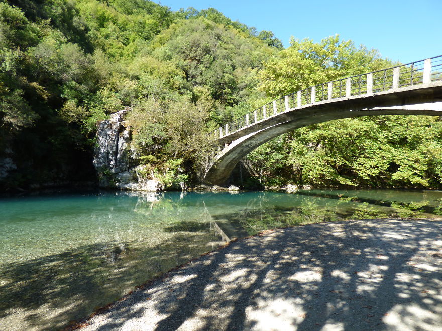 Arch bridge over crystal clear water surrounded by lush greenery, a mystical bridge leading to another world.