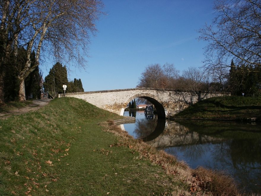 Stone arch bridge over calm river surrounded by grass and trees, a mystical bridge in a peaceful natural setting