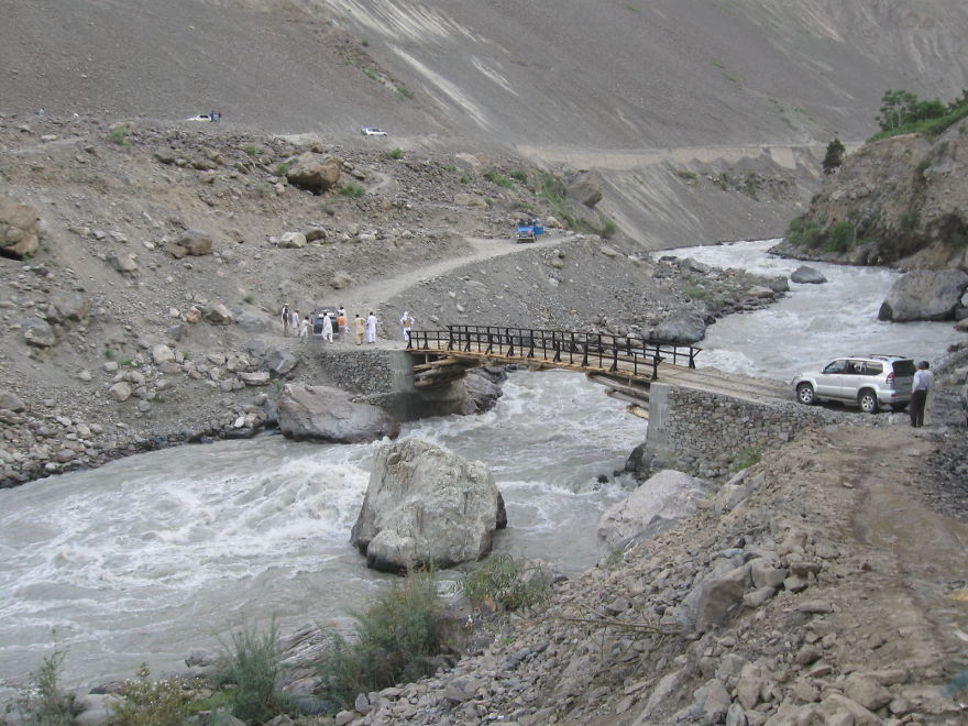 Rustic wooden bridge over a flowing river in a mountainous landscape, showcasing mystical bridges in remote natural settings.