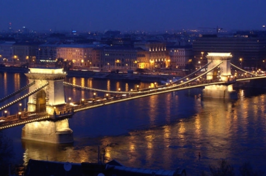 Illuminated mystical bridge over a river at night, reflecting city lights in a serene urban setting.