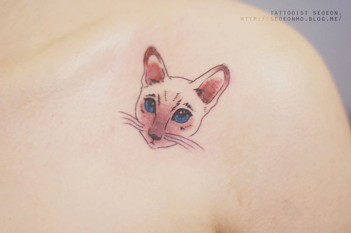 Minimalistic tattoo by Seoeon of a cat's face on the shoulder, showcasing feminine and discreet design. Minimalistic tattoo by Seoeon of a cat's face on the shoulder, showcasing feminine and discreet design.